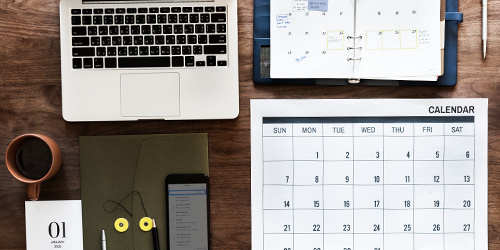 Skrivebord med laptop, kaffekop, kalender og notesbog